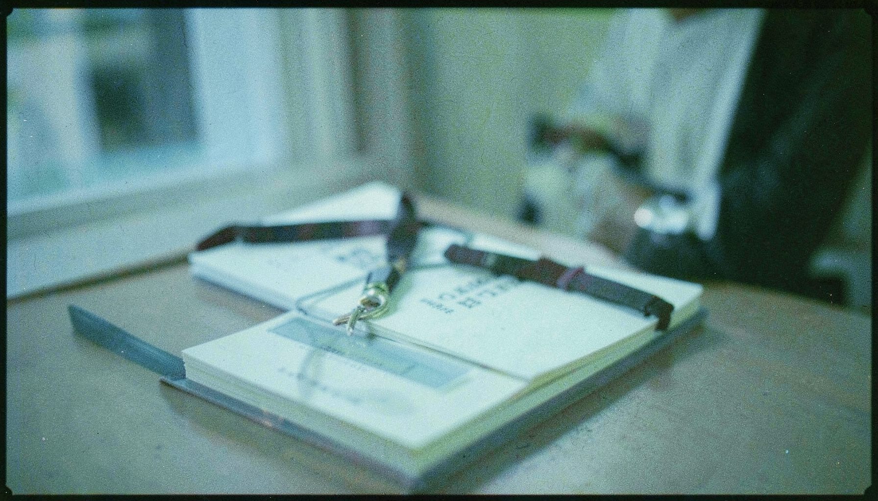 An analog film photograph of an ID holder with a lanyard draped over a notebook, soft office lighting, muted blues and grays.